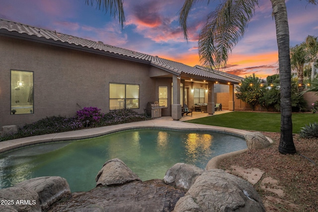 pool at dusk featuring a yard and a patio