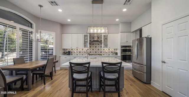kitchen with appliances with stainless steel finishes, decorative light fixtures, an island with sink, and white cabinets
