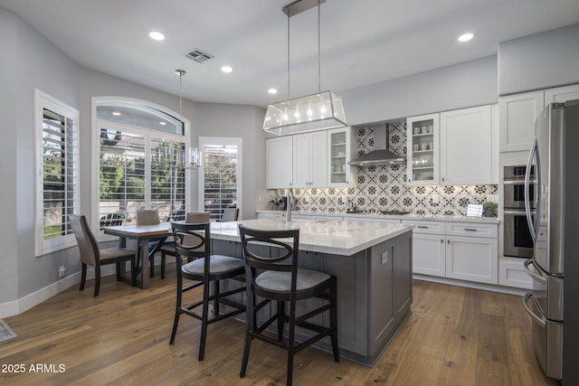 kitchen featuring white cabinetry, a kitchen island with sink, pendant lighting, and wall chimney exhaust hood