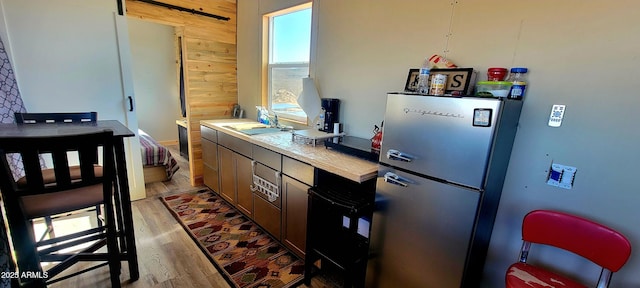 kitchen with a sink, tile countertops, a barn door, freestanding refrigerator, and wood finished floors