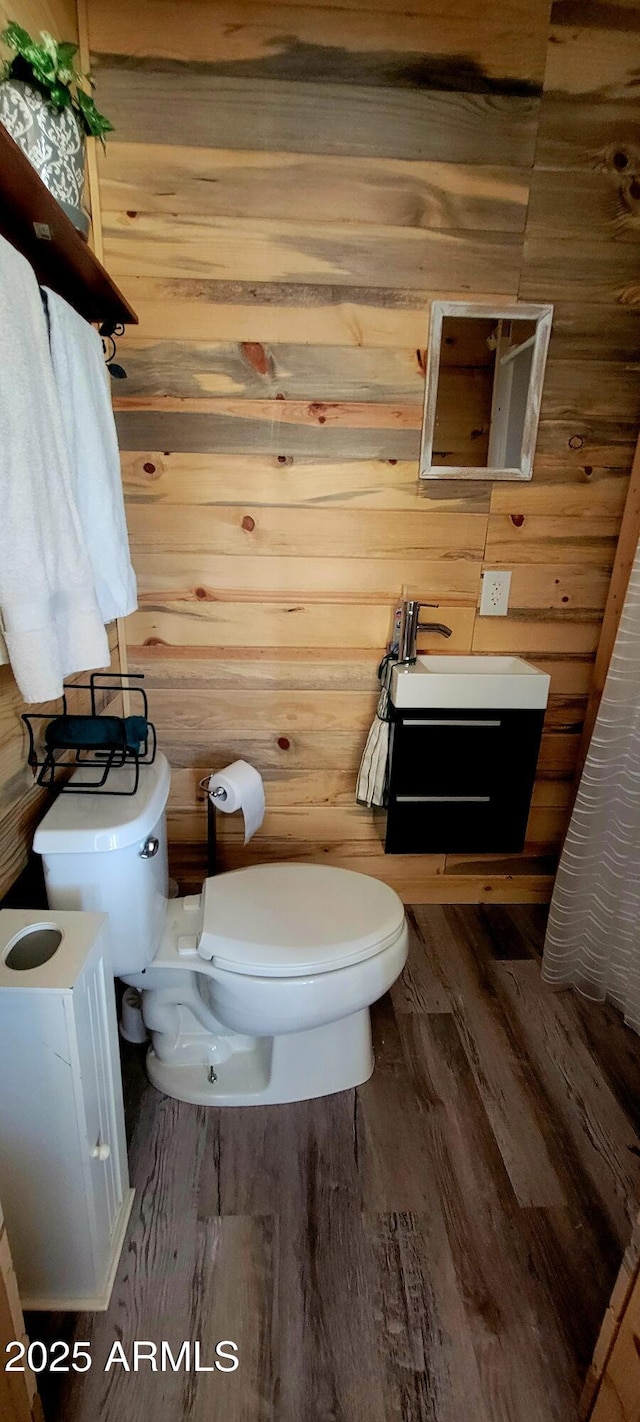 half bathroom featuring wood walls, toilet, and wood finished floors