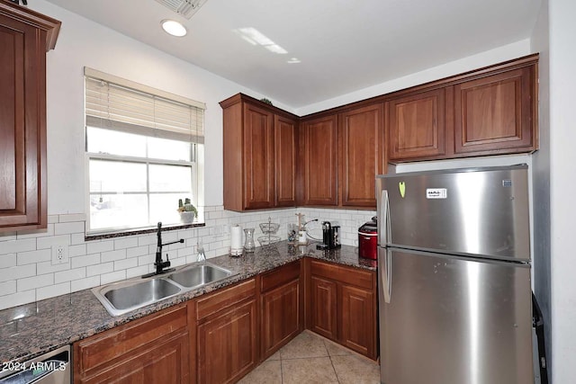 kitchen featuring light tile patterned floors, sink, backsplash, stainless steel appliances, and dark stone countertops