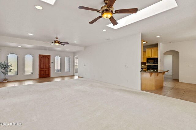 unfurnished living room with a skylight, light tile patterned floors, light colored carpet, and recessed lighting