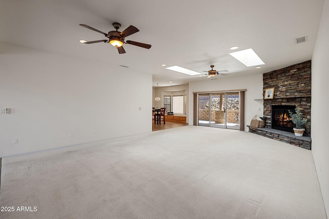 unfurnished living room with a skylight, visible vents, a stone fireplace, and carpet