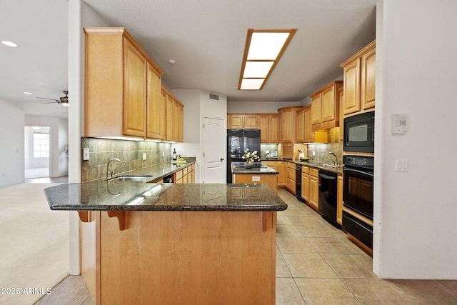 kitchen with dark stone countertops, a peninsula, a sink, black appliances, and backsplash