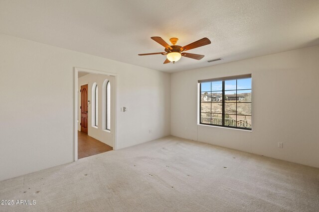 carpeted empty room featuring visible vents, a textured ceiling, and a ceiling fan