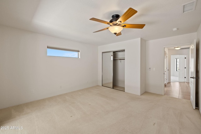 unfurnished bedroom featuring multiple windows, light colored carpet, visible vents, and a closet