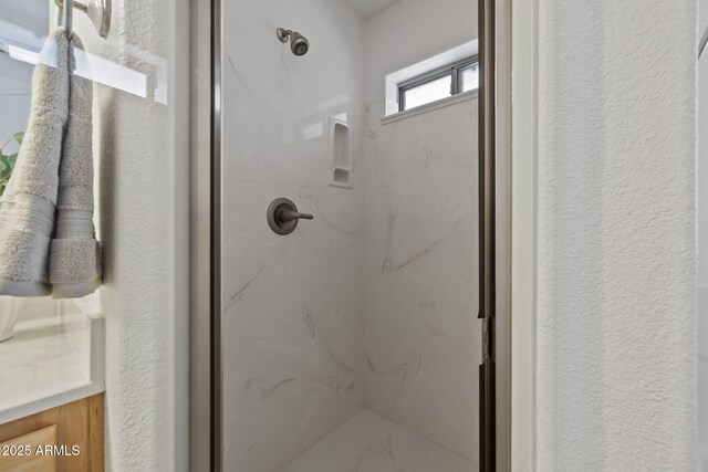 full bathroom featuring a marble finish shower and a textured wall