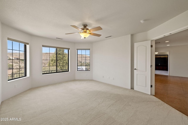 carpeted empty room with visible vents, a textured ceiling, and a ceiling fan