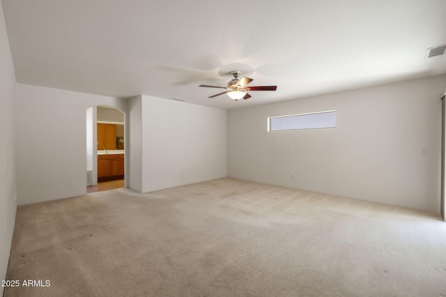 empty room with visible vents, arched walkways, light carpet, and a ceiling fan