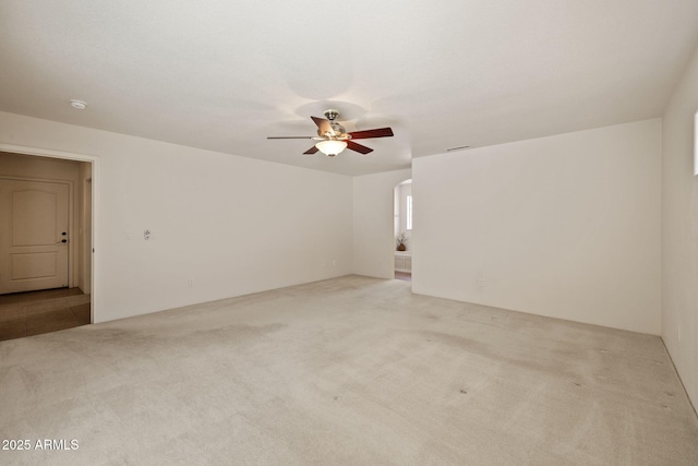 carpeted spare room featuring arched walkways and ceiling fan