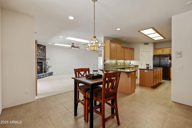 dining room with light carpet, a ceiling fan, recessed lighting, a stone fireplace, and light tile patterned flooring