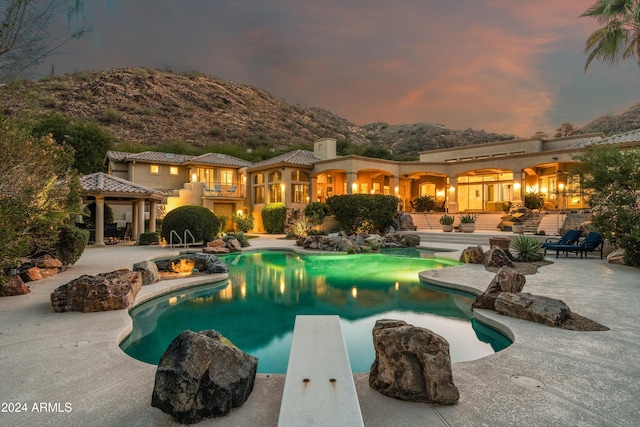 pool at dusk with a patio and a diving board