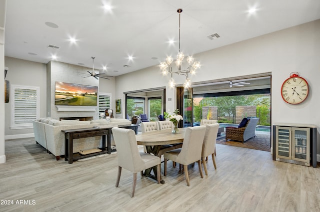 dining area with light wood-type flooring, a tile fireplace, and ceiling fan with notable chandelier