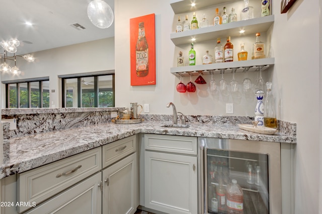 bar featuring beverage cooler, sink, and light stone counters