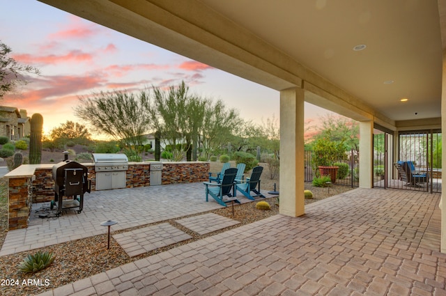 patio terrace at dusk featuring area for grilling and an outdoor kitchen