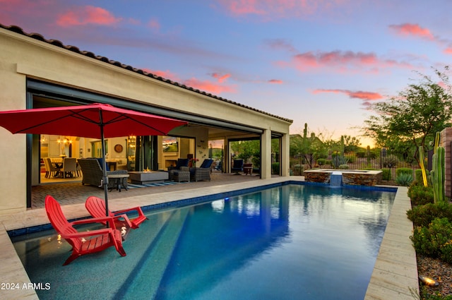 pool at dusk featuring a patio, an outdoor living space, and an in ground hot tub