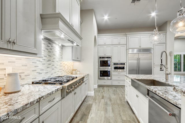 kitchen featuring light stone counters, pendant lighting, white cabinets, light hardwood / wood-style flooring, and appliances with stainless steel finishes