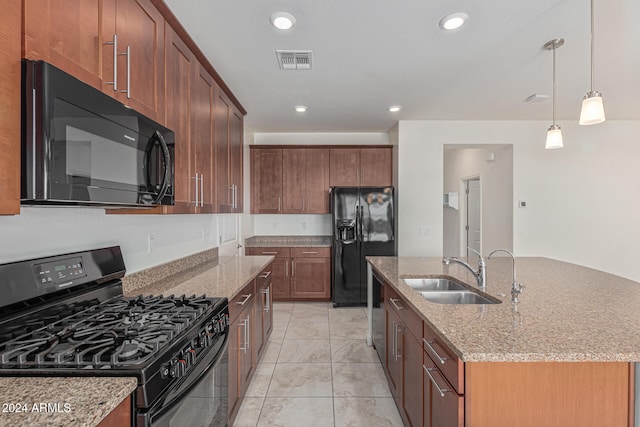 kitchen featuring a center island with sink, light stone counters, hanging light fixtures, black appliances, and sink