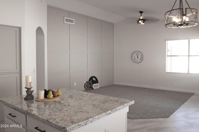 kitchen with decorative light fixtures, white cabinetry, a center island, light colored carpet, and ceiling fan with notable chandelier