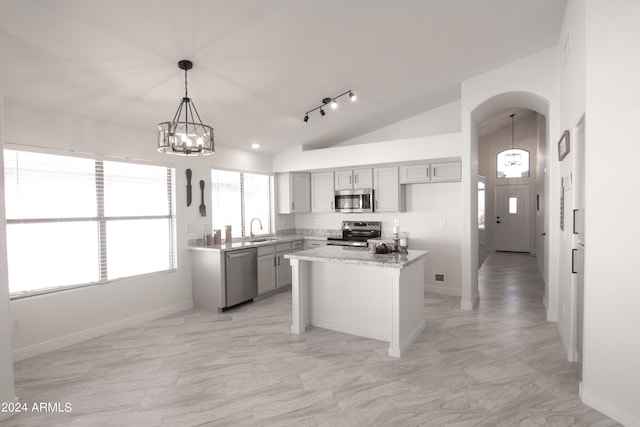 kitchen featuring sink, a kitchen island, appliances with stainless steel finishes, light stone countertops, and vaulted ceiling