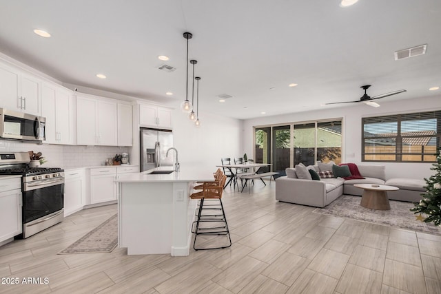 kitchen featuring a kitchen island with sink, white cabinets, hanging light fixtures, a breakfast bar area, and stainless steel appliances