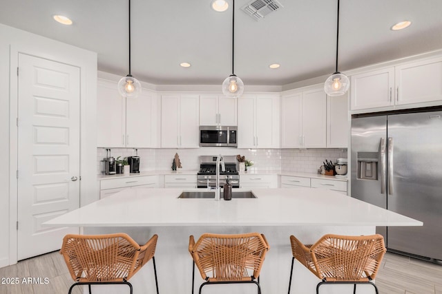 kitchen with appliances with stainless steel finishes, an island with sink, hanging light fixtures, and sink