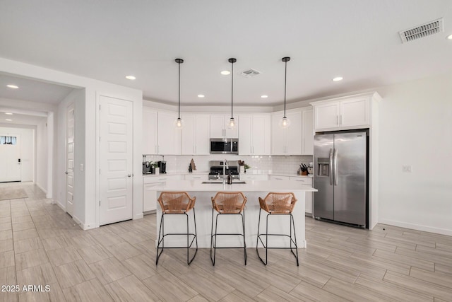 kitchen featuring appliances with stainless steel finishes, a center island with sink, white cabinetry, and hanging light fixtures