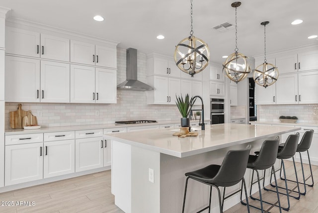 kitchen featuring gas cooktop, visible vents, a sink, light countertops, and wall chimney exhaust hood