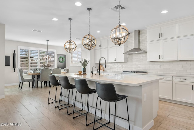 kitchen featuring visible vents, backsplash, gas stovetop, and wall chimney range hood