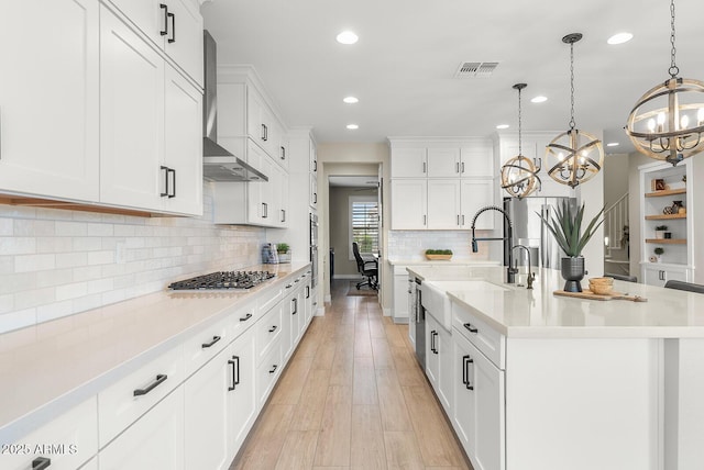 kitchen with visible vents, light countertops, light wood-type flooring, white cabinets, and wall chimney exhaust hood