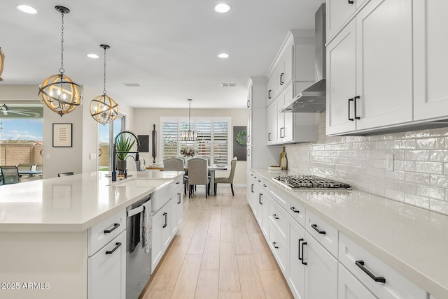 kitchen with visible vents, backsplash, wall chimney range hood, light countertops, and appliances with stainless steel finishes