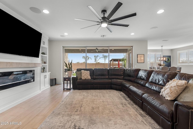 living room with visible vents, a ceiling fan, a glass covered fireplace, recessed lighting, and light wood-style floors