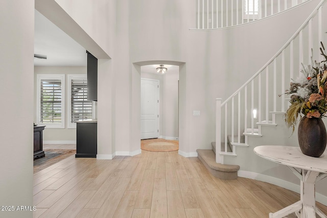 foyer with light wood finished floors, arched walkways, a high ceiling, and baseboards