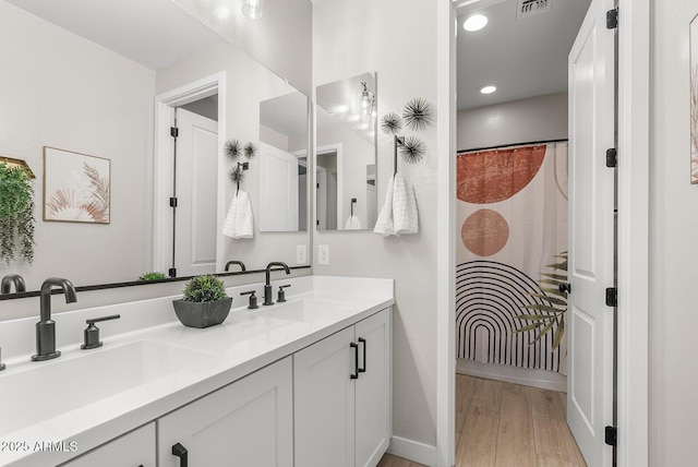 full bath featuring double vanity, wood finished floors, baseboards, and a sink