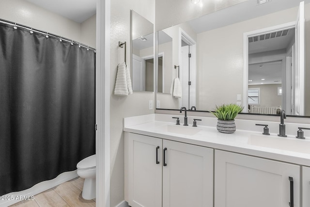 bathroom with double vanity, wood finished floors, toilet, and a sink