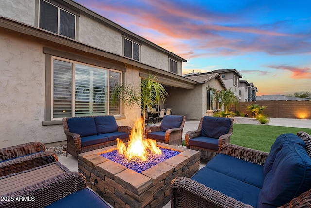 patio terrace at dusk featuring an outdoor living space with a fire pit and fence