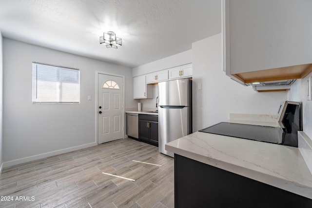 kitchen featuring appliances with stainless steel finishes, white cabinets, light stone countertops, a textured ceiling, and light wood-type flooring