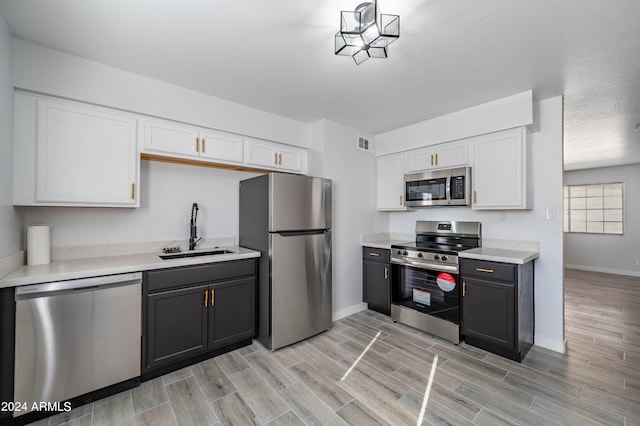 kitchen with appliances with stainless steel finishes, light hardwood / wood-style floors, white cabinetry, an inviting chandelier, and sink