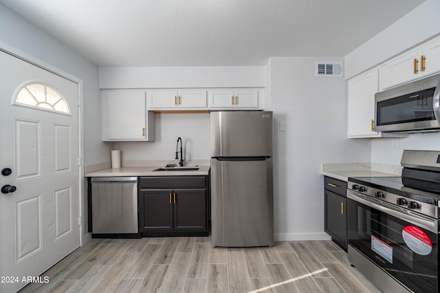 kitchen with appliances with stainless steel finishes, white cabinetry, sink, and light hardwood / wood-style flooring