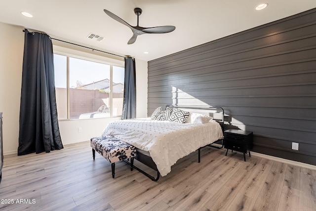 bedroom with ceiling fan, wood walls, and light wood-type flooring