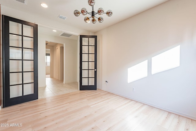 empty room featuring french doors, light hardwood / wood-style flooring, and a notable chandelier