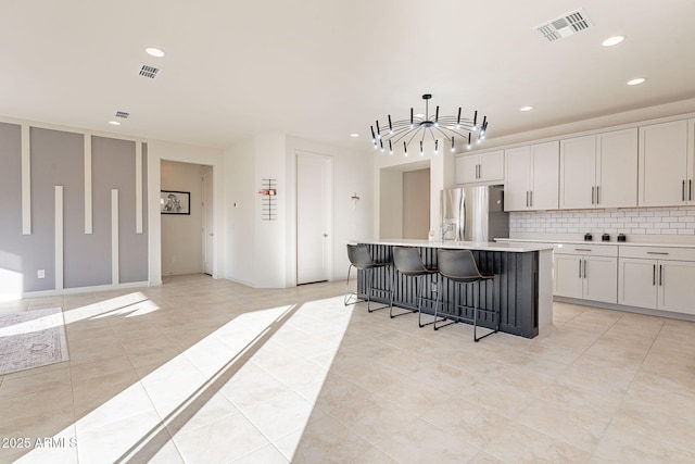 kitchen with stainless steel refrigerator with ice dispenser, pendant lighting, a center island with sink, white cabinets, and a breakfast bar area