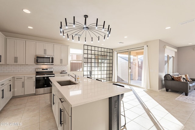 kitchen with appliances with stainless steel finishes, sink, light tile patterned floors, white cabinets, and an island with sink