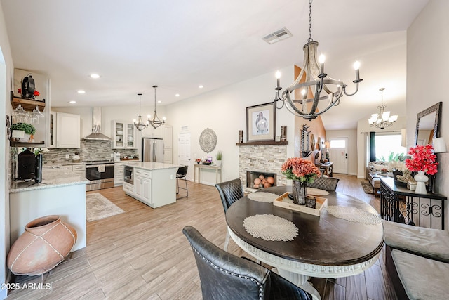 9085 E Windrose Dr, Scottsdale, AZ 85260 - dining room featuring a chandelier, a stone fireplace, light wood finished floors, and recessed lighting