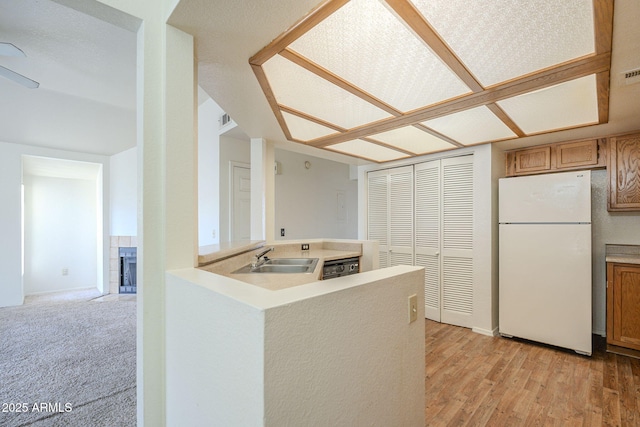 kitchen featuring a tile fireplace, freestanding refrigerator, light countertops, light wood-style floors, and a sink