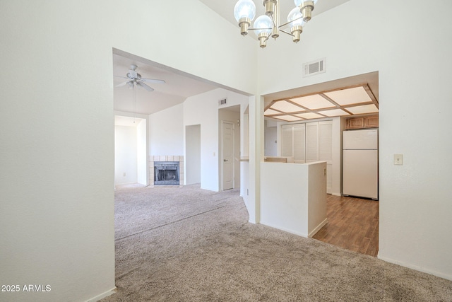 unfurnished living room with ceiling fan with notable chandelier, light colored carpet, visible vents, and a tile fireplace