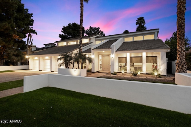 view of front of home featuring a tiled roof, an attached garage, fence, a yard, and stucco siding