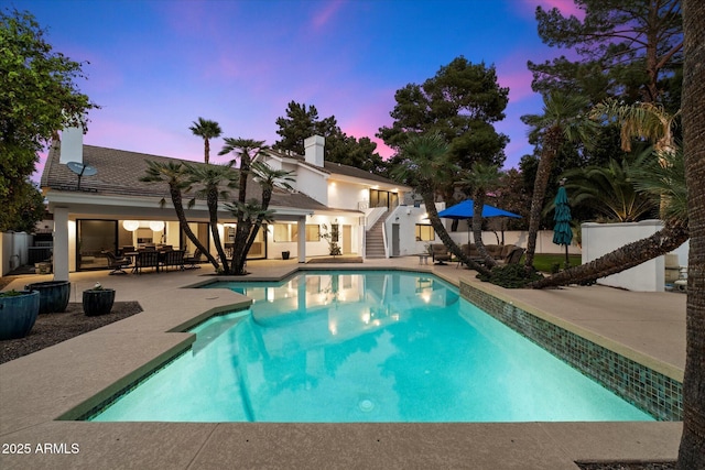 pool at dusk with outdoor dining space, stairway, a patio area, and an outdoor pool