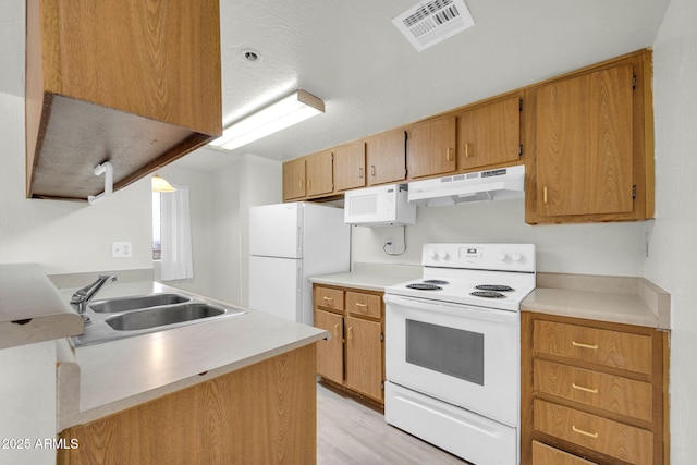 kitchen featuring visible vents, under cabinet range hood, light countertops, white appliances, and a sink